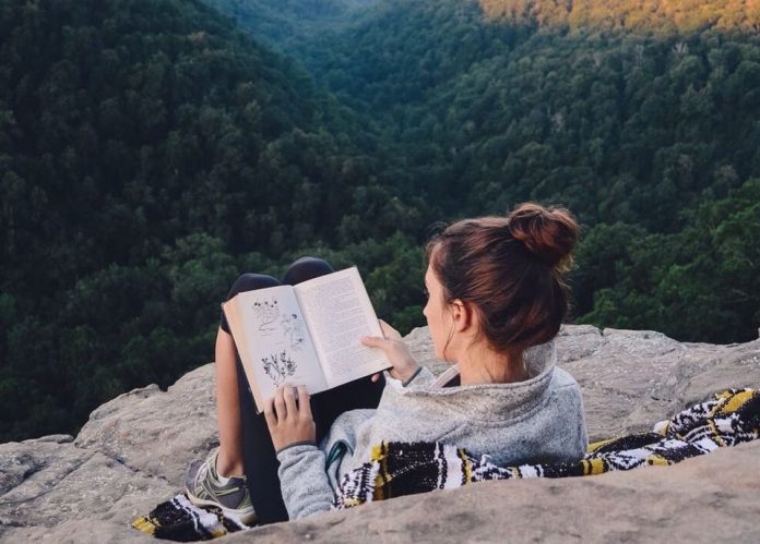 девушка читает книжку над утёсом